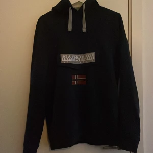 Mörkblå hoodie från Napapijri med tryck - Mörkblå hoodie från napapijiri. Sitter som en S och har en unik ficka.