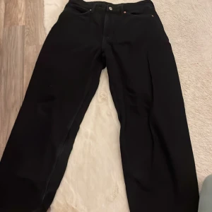 Svarta barrel jeans från A Denim - Svarta jeans från A Denim i barrel fit med hög midja. Modellen har breda ben och klassiska fem fickor, samt bälteshällor och knappstängning. Materialet är jeans och de har en stilren look som passar till sneakers eller boots.