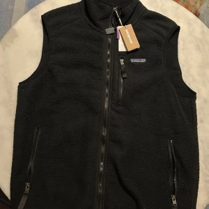 Svart fleeceväst från Patagonia - Patagonia Retro-X Fleece Vest – classic, warm and super high-quality fleece vest 🖤 Brand new with tags, never worn. Perfect for both city and outdoor wear – cozy, breathable, and functional. Original Patagonia item made from recycled materials.
