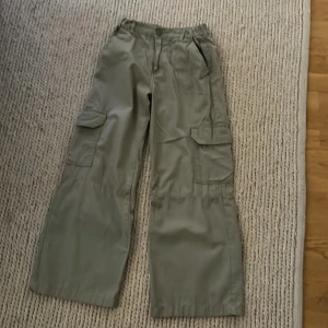 Gröna cargobyxor från H&M, stl 146 - Snygga gröna cargobyxor från H&M i storlek 146. Byxorna har breda ben, flera praktiska fickor på sidorna och bak, samt resår i midjan bak för extra komfort. Perfekta för en avslappnad och cool stil.
