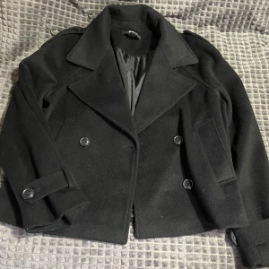 Svart kappa från Gina tricot - Superfin kappa från Gina Tricot i storlek S. Använd bara en gång, så den är i nyskick. Passar perfekt nu till hösten/vintern!!
