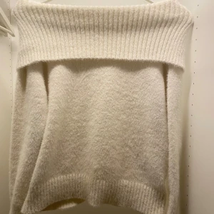 Offshoulder vit stickad tröja Lindex - Mysig offshoulder stickad tröja från Lindex i en ljusvit nyans. Tröjan har bred ribbad kant upptill och vid ärmslut, samt en fluffig och mjuk känsla. Perfekt för dig som gillar en avslappnad och trendig stil.