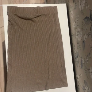 Beige ribbad kjol från 157 - En beige ribbad kortkjol från 157, perfekt för dig som gillar enkel och stilren design. Kjolen är stretchig och har en rak passform som sitter snyggt på kroppen. Materialet är mjukt och bekvämt, vilket gör den lätt att bära hela dagen.