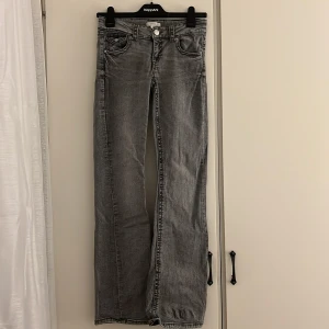 Grå bootcut jeans från Gina Tricot - Snygga grå jeans från Gina Tricot i bootcut-modell med klassiska fem fickor och silverfärgad knapp. Jeansen har en låg midja och raka ben med lätt utsvängd form. Materialet är slitstarkt denim och färgen är en cool, tvättad grå ton.