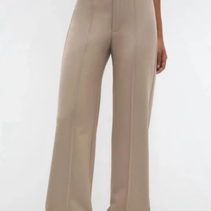 Beige wide kostymbyxor från H&M - Snygga beige kostymbyxor från H&M med hög midja och breda ben. Byxorna har klassiska pressveck framtill, bälteshällor och fickor. Perfekt för dig som gillar en clean och stilren look med lite extra edge.