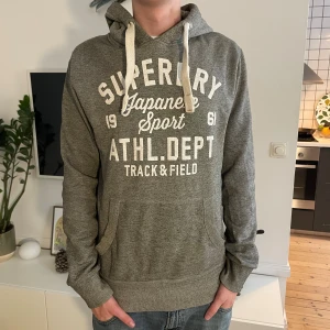 Grå hoodie från Superdry med tryck - Snygg grå superdry hoodie. Modellen är 187. Nypris 1500! Hör av dig vid minsta fundering🤗