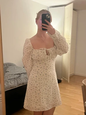 Blommig klänning - En kort vit klänning med blommor på och puffärmar från H&M. Endast använd tre gånger, går ungefär till mitten av låren/ovanför mina knän