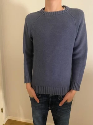 Blå stickad tröja med rund hals - Snygg blå stickad tröja med rundad hals och ribbade muddar vid ärmslut och nederkant. Tröjan har en enkel, clean look och är långärmad. Perfekt för dig som gillar stilrena plagg med lite struktur i materialet.