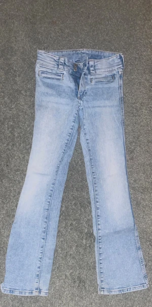 Bootcut ljusblå jeans med låg midja - Snygga ljusblå jeans med bootcut passform och låg midja. Jeansen har klassiska fickor framtill och bälteshällor. Materialet är jeans med en lätt tvättad look som ger en fräsch vibe. Perfekta för dig som gillar en avslappnad stil. Säljer pga av förkorta. Skulle passa någon mellan 145-160 cm!
