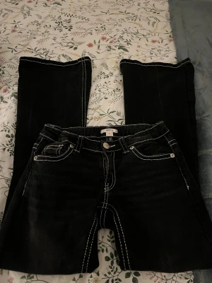 Svarta bootcut jeans från Gina Tricot - Svarta jeans från Gina Tricot i storlek 164 med kontrasterande vit söm och snygga broderade detaljer på bakfickorna. Modellen har bootcut-ben och klassisk femficksdesign. Jeansen är tillverkade i jeansmaterial och har normal passform. Säljer då det är lite för korta för mig som är ungefär 170cm. 💕