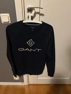 Svart sweatshirt från GANT - Svart sweatshirt från GANT med stort broderat logotyptryck i vitt på bröstet. Tröjan är i nytt skick använd en gång storlek S. Hör av dig vid minsta fundering 