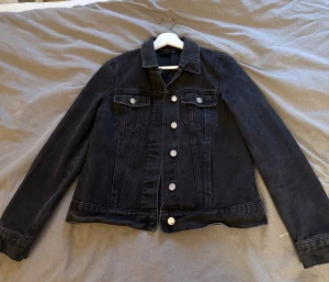 Svart jeansjacka  - Snygg svart jeansjacka med klassisk krage och raka linjer. Jackan har silverfärgade knappar framtill och två bröstfickor med lock. Perfekt att slänga på över en hoodie eller t-shirt för en chill look. Köpt på Veronmoda för cirka 2-3 år sedan men har inte andvändt den så mycket💕💕Pris går självklart att diskutera.