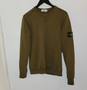 sweatshirt från Stone Island - Säljer en  långärmad sweatshirt från Stone Island med klassisk patch på vänster ärm. Tröjan har rund halsringning och ribbade muddar vid ärmslut och nederkant. Perfekt för dig som gillar streetwear och snygga basplagg. Se bilder för skick. 