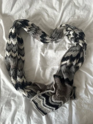Grå/svart halsduk från Missoni - Snygg stickad halsduk med klassiska zigzag-mönster i svart, grått och vitt samt med lite glitter trådar. Mjuk och varm, perfekt för kyliga dagar. Lång och bred modell som kan stylas på flera sätt. Passar dig som gillar grafiska mönster och neutrala färger                                             Längd: ca 190cm Bredd: ca 40cm