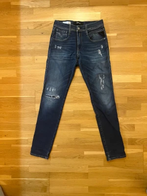 Replay Anbass Hyperflex jeans med slitningar - Snygga Replay Anbass Hyperflex jeans i mörkblå tvätt med slitningar och distressed detaljer. Stretchigt material för extra komfort. Storlek W29 L32