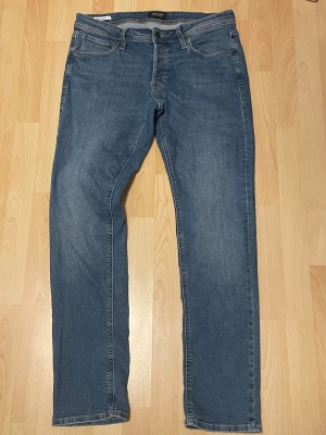Slim Glenn blå jeans från Jack & Jones 32/34 - Snygga blå jeans från Jack & Jones i modellen Slim Glenn. Klassisk femficksdesign, slim passform och raka ben. Jeansen har normal midja och är tillverkade i mjukt denimtyg med lätt tvättad look. Perfekt för dig som gillar stilrena och bekväma jeans.