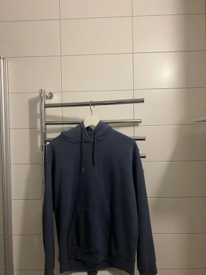 Mörktukås  hoodie från RYVLS med huva - Säljer en stilren blå hoodie från RYVLS i storlek 158/164. Tröjan har huva med snörning och en stor magficka framtill. Perfekt för dig som gillar en enkel och avslappnad look. Materialet är mjukt och skönt, passar till många tillfällen.