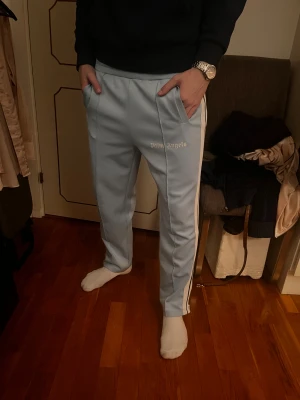 Palm angels byxor - Dessa ljusblå Palm Angels track pants är både stilrena och bekväma. Med sina vita ränder längs sidorna ger de en sportig men ändå trendig look. Perfekta för en avslappnad dag eller för att piffa upp en enklare outfit! Ända defekten är en fett fläck som finns på bild 4 men inget som finns vid användning. Dessa byxor är även äkta! Skriv vid frågor eller funderingar😊