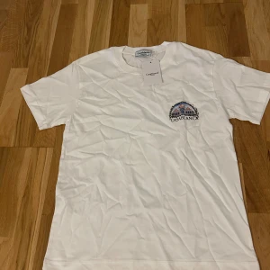 Vit t-shirt från Casablanca Tennis Club - Snygg vit t-shirt från Casablanca Tennis Club med färgglad grafik på ryggen och broderad logga på bröstet. Klassisk rund hals och korta ärmar. Materialet är mjuk bomull som känns skönt mot huden. Perfekt för dig som gillar stilrena plagg med coola detaljer.