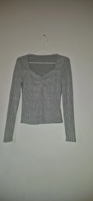 Ribbad stickad tröja v-ringad - Snygg grå stickad tröja med ribbad struktur och v-ringad hals. Modellen är långärmad och har en smickrande passform som sitter normalt. Perfekt att matcha med jeans eller kjol för en chill look.