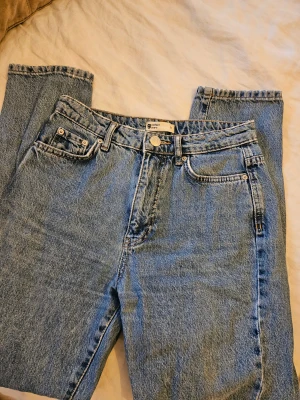 Gina tricot jeans i ljusblå denim - Säljer ett par klassiska ljusblå jeans från Perfect Jeans (Gina trico) med, raka ben och hög midja. Jeansen har en snygg vintage-vibe och är tillverkade i slitstark bomullsdenim. Passar dig som gillar tidlös stil och enkel design.