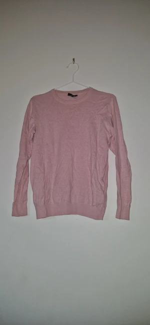 Ljusrosa stickad tröja - En enkel och snygg ljusrosa stickad tröja från Smog i storlek XS. Tröjan har rund hals, långa ärmar och ribbade muddar vid ärmslut och nederkant. Perfekt för dig som gillar en clean och soft look.