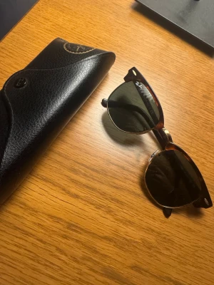 Ray-Ban Clubmaster solglasögon brun - ‼️PRISET ÄR FÖRHANDLINGSBART‼️ Snygga Ray-Ban Clubmaster solglasögon med klassisk brunmelerad båge och guldiga detaljer. Glasen är mörka och har en rundad form som ger en retro vibe. Kommer med original svart fodral med Ray-Ban-logga i guld. Perfekt för dig som vill ha en ikonisk look.