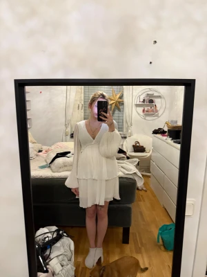 Vit omlottklänning med volang - Supersöt vit kortklänning med omlott och v-ringning. Klänningen har långa, vida ärmar och volangdetaljer i nederkant. Perfekt för sommarens alla tillfällen och ger en romantisk vibe.