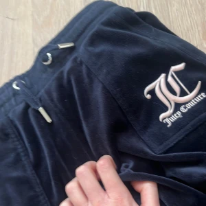 Mörkblåa  Juicy Couture 8/9 - Mörkblå mjukisbyxor från Juicy Couture i velour med snörning i midjan och silverfärgade detaljer. Klassisk JC-logga broderad på fickan. Byxorna har normal passform och bootcut-ben, perfekta för en chill och trendig look.