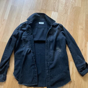 Svart Saint Laurent overshirt - Svart overshirt från Saint Laurent Paris i mjuk bomull. Klassisk krage, långärmad med knappstängning och rå kant nedtill. Patch med 'Property of Saint Laurent' på bröstet och en bröstficka. .