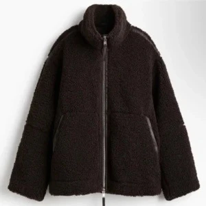 Mörkbrun teddyjacka med dragkedja - Säljer en mörkbrun teddyjacka med hög krage och grov dragkedja framtill. Jackan har två sidofickor och är i en loose passform, perfekt för att hålla sig varm. Materialet är mjuk fleece och jackan har långa ärmar för extra mysfaktor.