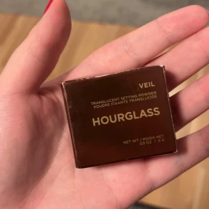 Hourglass Veil Translucent Setting Powder - Hourglass Veil Translucent Setting Powder i en lyxig, brun metallic förpackning. Puderet är transparent och ger en silkeslen finish som fixerar sminket utan att kännas tungt. Perfekt för att matta ner och ge en flawless look. 0,9 gram
