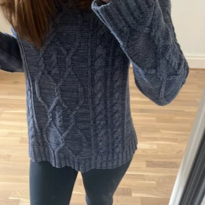 Mörkblå stickad kabeltröja - Säljer en mörkblå stickad tröja med grovt kabelmönster och breda ribbade muddar. Tröjan har långärmade ärmar och en relaxed passform som är både chill och snygg. Perfekt för dig som gillar mysiga och stilrena plagg. Den är o storlek M men passar även mig som brukar ha S eller XS