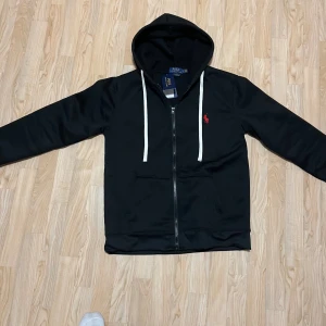 Svart hoodie Ralph Lauren - Svart Ralph Lauren kofta i helt nytt skick med tag och i storlek L men passar även för M, jag är M och den passar mig.