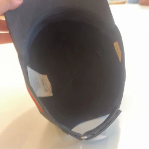 Svart Gucci keps med röd/grön rand - Snygg svart keps från Gucci med diskret GG-mönster över hela kepsen och klassisk röd/grön rand på sidan. Justerbar rem baktill för perfekt passform. Materialet är bomull och kepsen har en stilren och modern look som sticker ut.