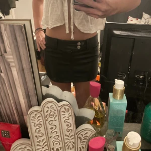 Svart minikjol i skinnimitation - Säljer en svart kortkjol i skinnimitation med två knappar framtill och klassiska fickor. Kjolen har en tight passform och är perfekt för dig som gillar en edgy och trendig stil. Passar till crop tops och boots.