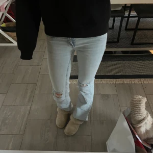Ljusblå bootcut jeans med slitningar - Säljer ett par ljusblå jeans från nelly med bootcut passform och snygga slitningar vid knäna. Jeansen har klassisk femficksdesign, rosa broderad detalj på bakfickan och är tillverkade i mjukt denimtyg. Använda fåtal gånger och är i storlek 34