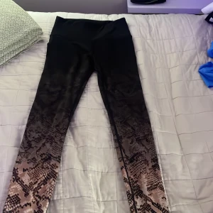 Svarta leggings med ormskinnsmönster XS - Snygga svarta leggings i storlek XS med coolt ormskinnsmönster som går från knäna och ner mot anklarna. Hög midja och stretchigt material som sitter skönt. Perfekta för dig som vill sticka ut med en unik look.