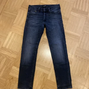 Slim Glenn mörkblå jeans 28/30 - Mörkblå jeans från Slim Glenn i slim fit-modell med klassisk femficksdesign. Jeansen har en snygg tvätt med lätt slitning och raka ben. Passar dig som gillar en smalare siluett och stilren look. Materialet är mjukt och stretchigt jeans.