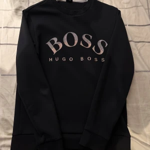 Svart sweatshirt från Hugo Boss - Svart sweatshirt från Hugo Boss med stor BOSS-logga på bröstet. Tröjan har rund halsringning, långa ärmar och ribbade muddar. kan gå ner i priset vid snabbt köp.