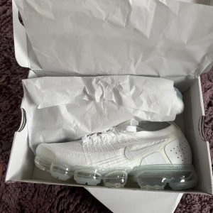 Nike Air Vapormax Flyknit 2 Vit, helt nya och oanvända. - Nike Air Vapormax Flyknit 2 i helvit färg med transparent sula. Skorna har stickad ovandel i flyknit-material, snörning och rund tå. Snygg och modern design med ventilerande mesh och ikonisk Swoosh-logga på sidan. Perfekt för dig som gillar sportiga sneakers med unik sula.