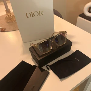 Dior solglasögon  - Snygga solglasögon från Christian Dior med transparent beige båge och fyrkantig form. Guldiga detaljer på skalmarna där det står 'Christian Dior'. Glasen är bruna med lätt toning. Perfekt accessoar för en trendig look.