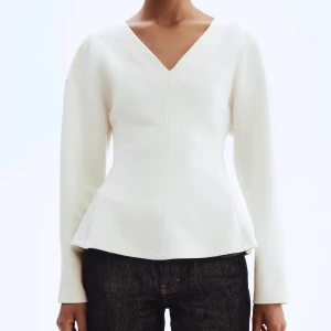Vit v-ringad långärmad topp - Stilren vit topp med v-ringning och långa ärmar. Modellen har en lätt utsvängd passform som ger en snygg siluett. Perfekt att matcha med jeans eller kjol för en clean look. Använd 1 gång. 