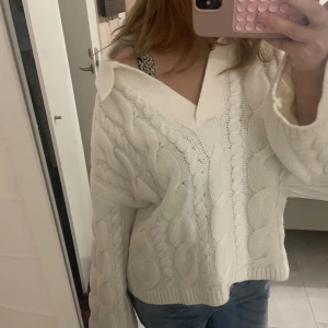 Vit stickad offshoulder tröja - Säljer en vit stickad tröja med grova kabelstickade detaljer och v-ringad design. Tröjan har en loose passform och långa ärmar, perfekt för att ge en chill och snygg vibe. Supermysig och passar till jeans eller kjol. S/M