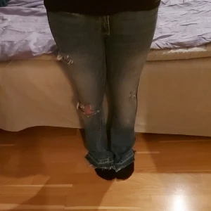 Blå bootcut jeans med slitningar - Säljer ett par blå bootcut jeans med snygga slitningar och hål på knäna. Jeansen har låg midja, och dubbla knappar i linningen. De har klassiska fickor både fram och bak. Perfekt för dig som gillar en trendig look. Meddela för frågor eller pris💞💞