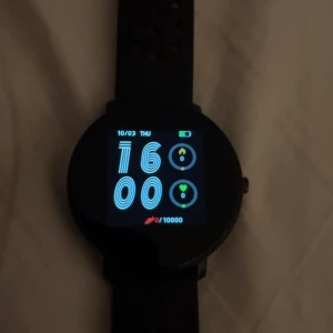 Svart smartklocka från Denver - Säljer en rund svart smartklocka från Denver med digital display och silikonarmband med hålmönster. Klockan har touchskärm, pulsmätare och stegräknare. Perfekt för dig som gillar teknik och vill ha koll på din aktivitet.