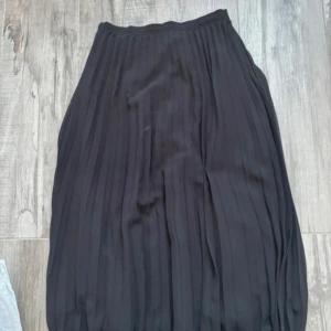 Svart plisserad långkjol Gina Tricot - Svart plisserad långkjol från Gina Tricot i storlek 36. Kjolen har ett snyggt, flowigt fall och bred linning. Perfekt för dig som gillar stilrena och klassiska plagg med lite edge. Materialet känns lätt och skönt mot huden.