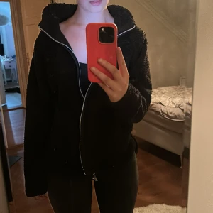 Svart teddyjacka med dragkedja - Mysig svart teddyjacka med huva och hel dragkedja framtill. Jackan har en fluffig och mjuk yta i fleece, långärmad och med avslappnad passform. Perfekt för kyliga dagar när du vill vara både bekväm och snygg. Skit snygg och mjuk men kommer inte till användning för mig längre 🥰 Jätte bra nu till vintern ‼️☺️