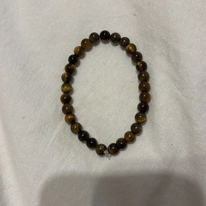 Brunt pärlarmband med tigeröga - Snyggt armband med runda pärlor av tigeröga i bruna och gyllene toner. Elastiskt band gör det enkelt att ta på och av. Perfekt accessoar för dig som gillar naturliga stenar och en jordnära stil.