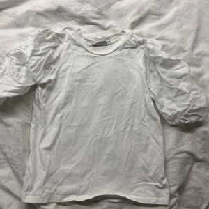Vit puffärmad topp från Kappahl XS - Säljer en vit topp från Kappahl i storlek XS. Toppen har puffiga korta ärmar som ger en trendig look och är tillverkad i mjuk bomull. Perfekt för dig som gillar stilrena och enkla plagg med en twist. Passar s